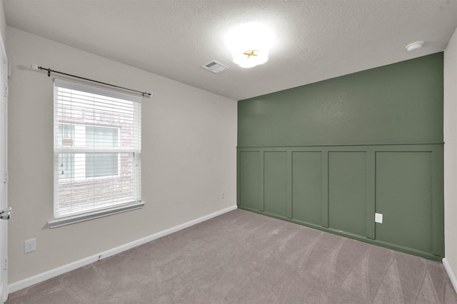 spare room with a textured ceiling, a decorative wall, light carpet, visible vents, and wainscoting