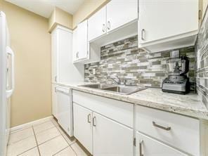 kitchen featuring light tile patterned floors, fridge, white dishwasher, white cabinets, and backsplash