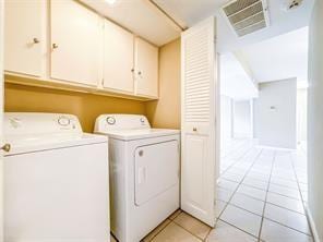 washroom with cabinets, washing machine and clothes dryer, and light tile patterned floors