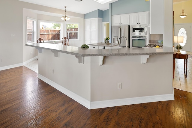 kitchen with a breakfast bar, decorative light fixtures, appliances with stainless steel finishes, dark hardwood / wood-style flooring, and white cabinets