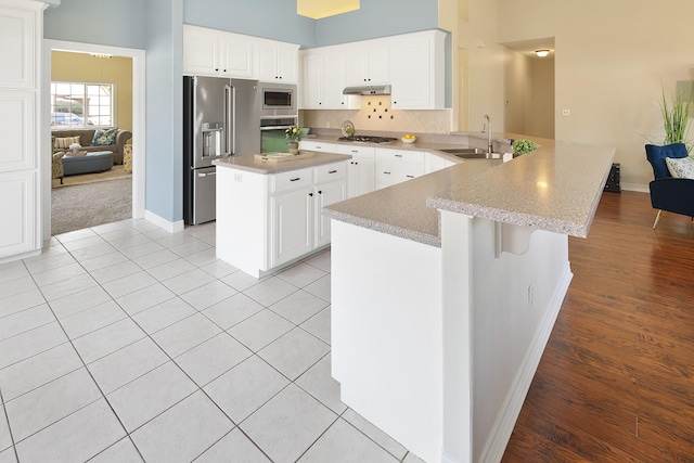 kitchen featuring sink, white cabinetry, stainless steel appliances, a kitchen island, and kitchen peninsula