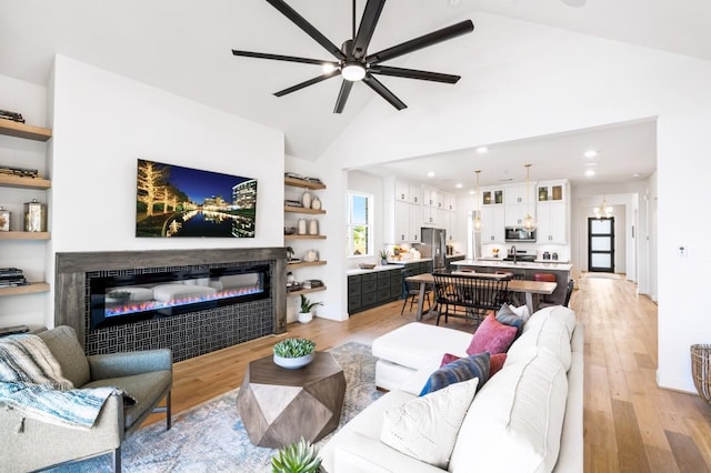 living room featuring ceiling fan, high vaulted ceiling, sink, and light hardwood / wood-style flooring