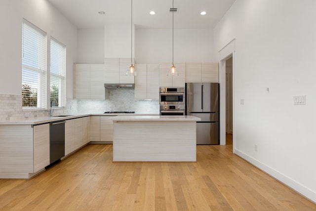 kitchen featuring sink, a towering ceiling, stainless steel appliances, a center island, and decorative light fixtures