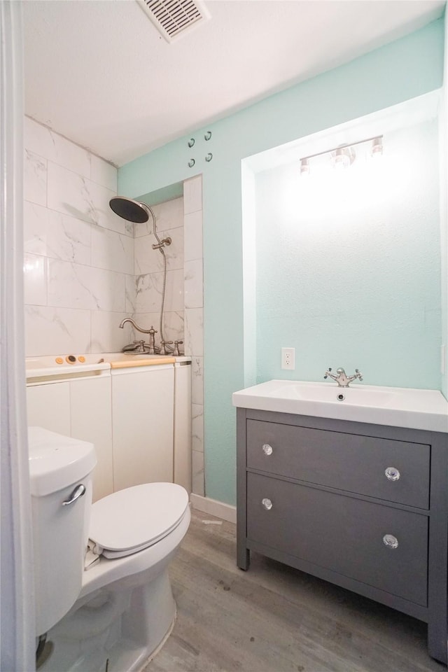 bathroom featuring vanity, tiled shower, hardwood / wood-style floors, and toilet