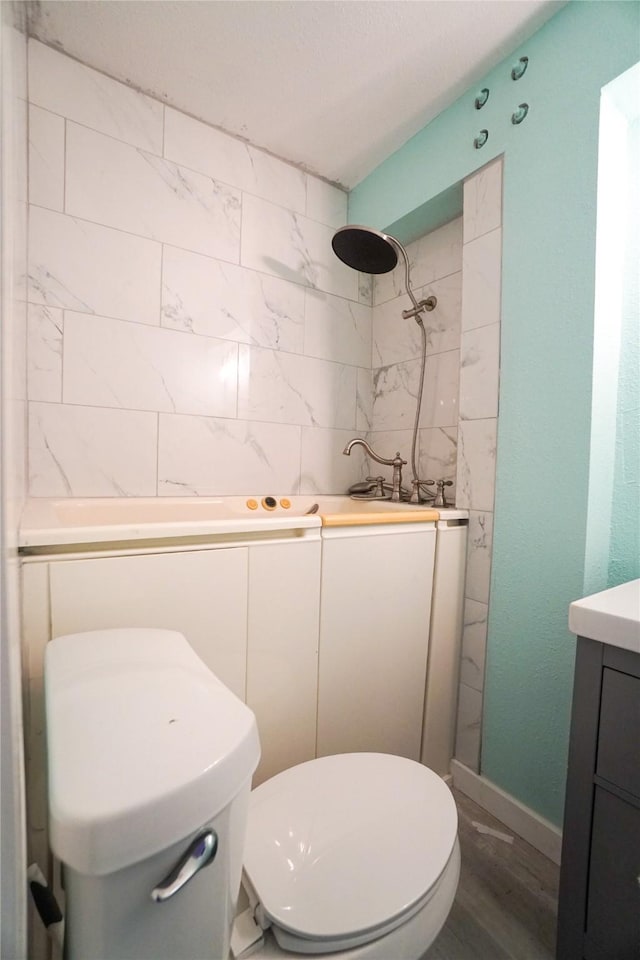 bathroom featuring hardwood / wood-style flooring, tiled shower, vanity, and toilet