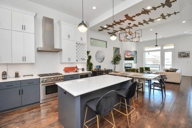 kitchen featuring gray cabinets, white cabinetry, hanging light fixtures, stainless steel range, and wall chimney exhaust hood