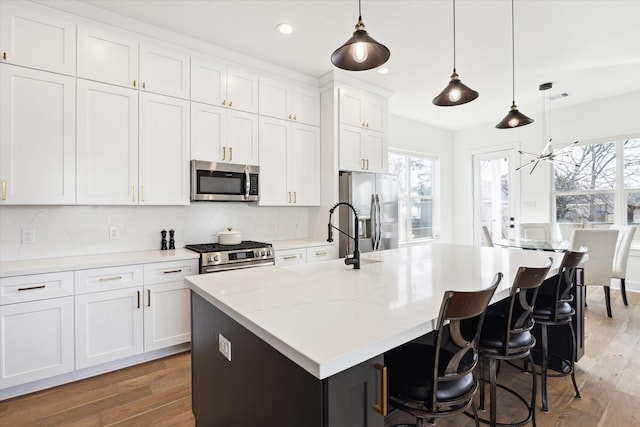 kitchen featuring pendant lighting, white cabinetry, stainless steel appliances, and an island with sink