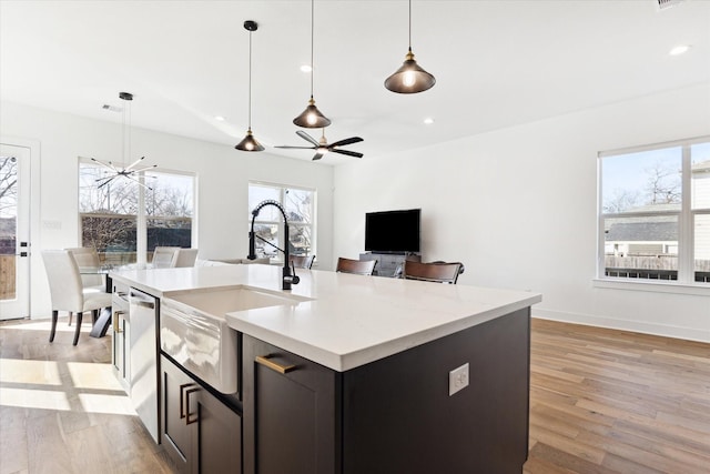 kitchen featuring an island with sink, sink, hanging light fixtures, stainless steel dishwasher, and light hardwood / wood-style flooring