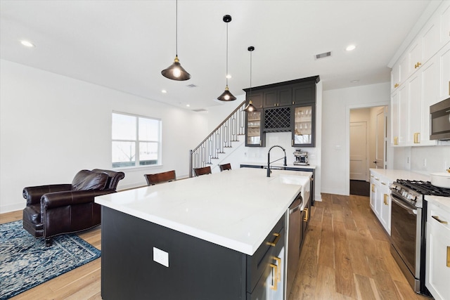 kitchen with white cabinetry, decorative light fixtures, appliances with stainless steel finishes, and a center island with sink