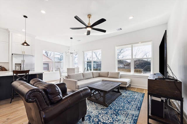 living room with ceiling fan with notable chandelier and light wood-type flooring