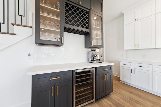 bar with wine cooler, white cabinets, and light wood-type flooring