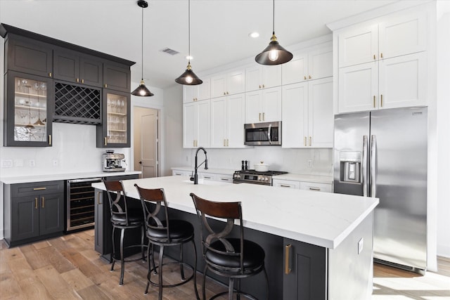 kitchen with pendant lighting, sink, appliances with stainless steel finishes, an island with sink, and beverage cooler