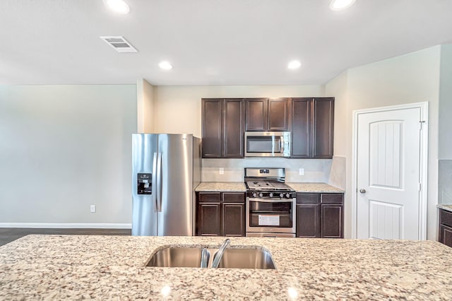 kitchen featuring light stone countertops, appliances with stainless steel finishes, sink, and dark brown cabinetry