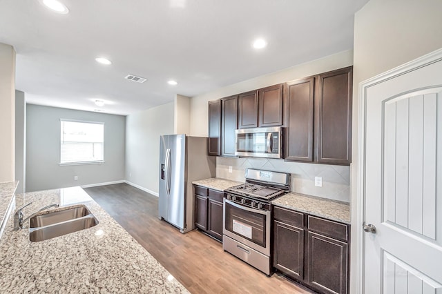 kitchen with sink, stainless steel appliances, light stone countertops, decorative backsplash, and light wood-type flooring