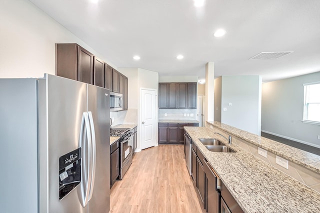 kitchen featuring sink, dark brown cabinetry, light stone counters, stainless steel appliances, and light hardwood / wood-style floors