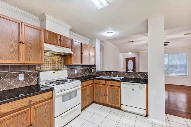 kitchen with light tile patterned flooring, tasteful backsplash, sink, dark stone counters, and white appliances