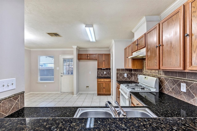 kitchen with sink, dark stone countertops, white range with gas stovetop, light tile patterned floors, and crown molding