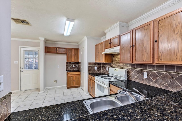 kitchen featuring white gas range, sink, decorative backsplash, dark stone counters, and light tile patterned floors