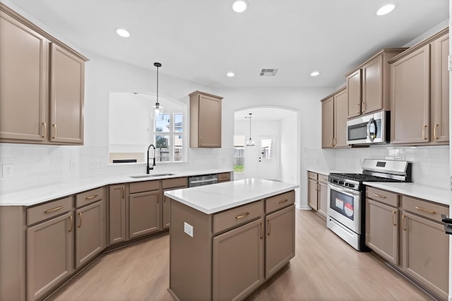 kitchen with appliances with stainless steel finishes, sink, light hardwood / wood-style flooring, and decorative light fixtures