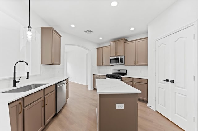 kitchen featuring sink, light hardwood / wood-style flooring, pendant lighting, stainless steel appliances, and backsplash