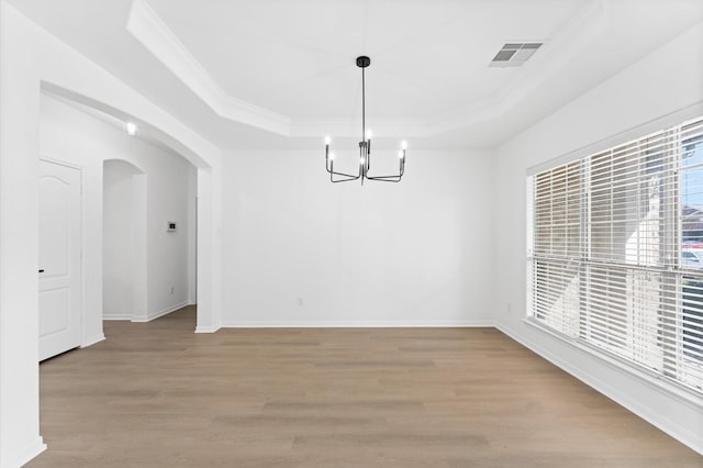 unfurnished dining area featuring an inviting chandelier, ornamental molding, light hardwood / wood-style floors, and a raised ceiling