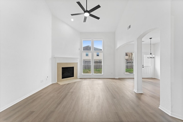 unfurnished living room featuring hardwood / wood-style floors, a towering ceiling, ceiling fan with notable chandelier, and a tile fireplace