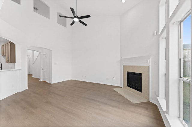 unfurnished living room featuring a fireplace, light hardwood / wood-style floors, ceiling fan, and a high ceiling