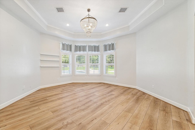 empty room with a raised ceiling, ornamental molding, a chandelier, and light wood-type flooring