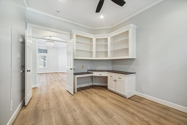 unfurnished office featuring crown molding, built in desk, ceiling fan, and light wood-type flooring