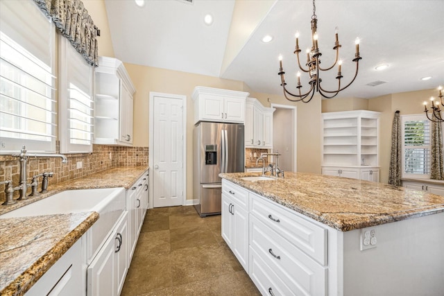 kitchen featuring stainless steel refrigerator with ice dispenser, sink, white cabinetry, light stone counters, and a kitchen island with sink