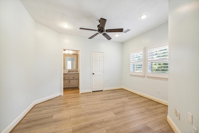 unfurnished bedroom featuring ceiling fan, ensuite bath, a textured ceiling, and light wood-type flooring