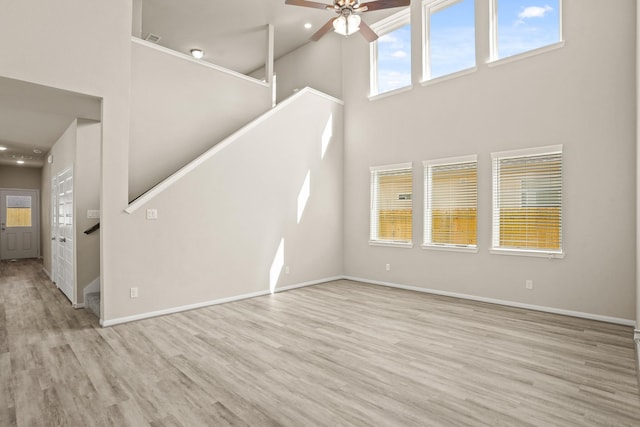 unfurnished living room featuring ceiling fan, a towering ceiling, and light hardwood / wood-style floors