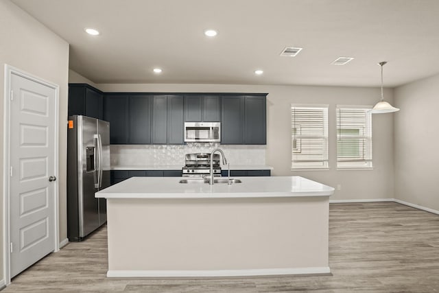 kitchen with sink, hanging light fixtures, stainless steel appliances, and an island with sink