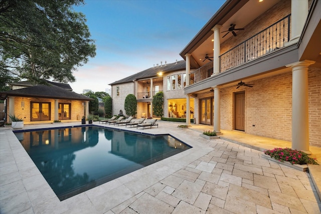 pool at dusk with an outbuilding, a patio area, and ceiling fan