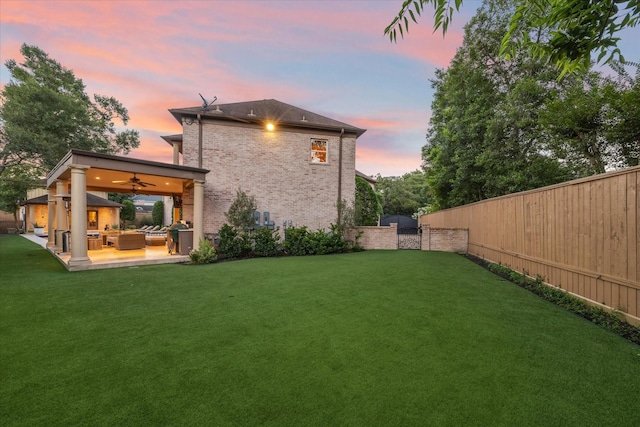 back house at dusk with outdoor lounge area, a patio area, ceiling fan, and a lawn