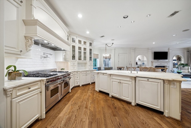 kitchen with a kitchen island with sink, sink, range with two ovens, and white cabinets