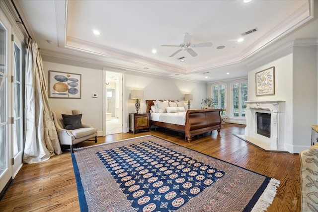 bedroom with crown molding, a tray ceiling, wood-type flooring, and a premium fireplace