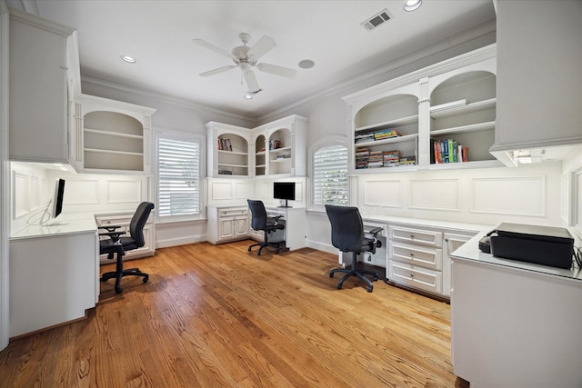 office space featuring built in desk, ornamental molding, ceiling fan, light wood-type flooring, and built in shelves