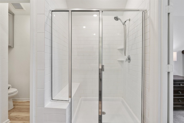 bathroom with wood-type flooring, a shower with door, and toilet