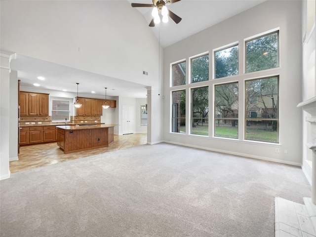 unfurnished living room with ornate columns, a wealth of natural light, light carpet, and ceiling fan