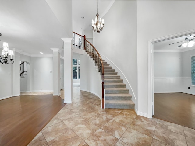 foyer entrance featuring a towering ceiling, ceiling fan with notable chandelier, ornamental molding, and light tile patterned flooring