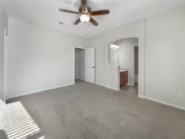 interior space with connected bathroom, light colored carpet, and ceiling fan