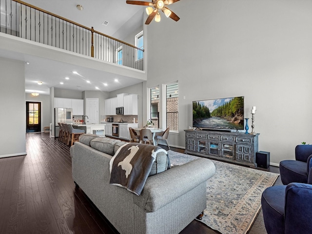 living room with dark hardwood / wood-style floors, sink, ceiling fan, and a towering ceiling