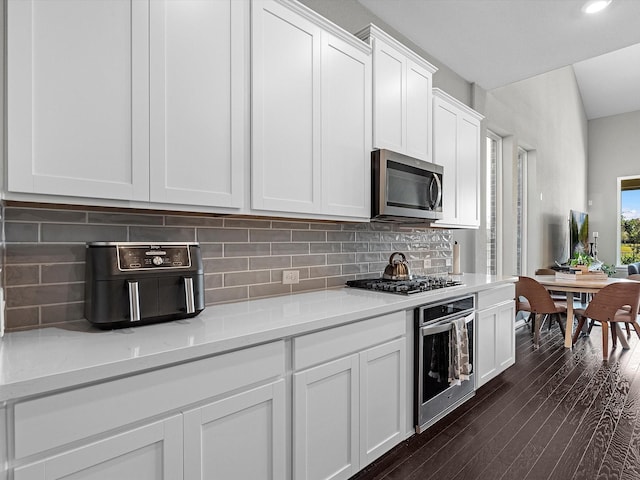 kitchen with appliances with stainless steel finishes, light stone counters, white cabinets, dark hardwood / wood-style flooring, and decorative backsplash