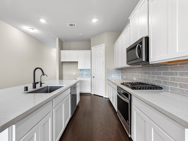 kitchen with sink, appliances with stainless steel finishes, light stone countertops, white cabinets, and dark hardwood / wood-style flooring