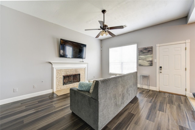 living room featuring dark wood-type flooring, ceiling fan, and a tile fireplace