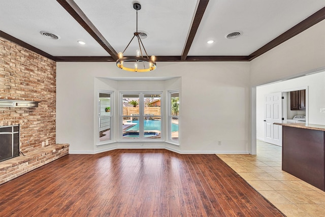 unfurnished living room with a notable chandelier, beam ceiling, a fireplace, and light wood-type flooring