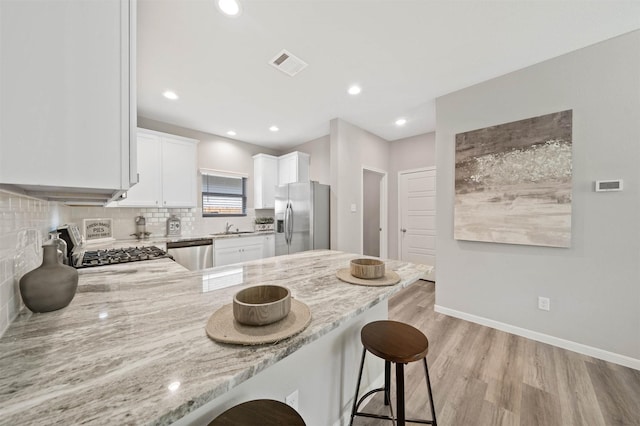 kitchen with light stone counters, tasteful backsplash, stainless steel appliances, light hardwood / wood-style floors, and white cabinets