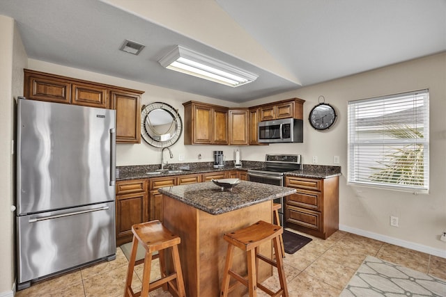 kitchen featuring light tile patterned flooring, a kitchen bar, sink, a kitchen island, and stainless steel appliances