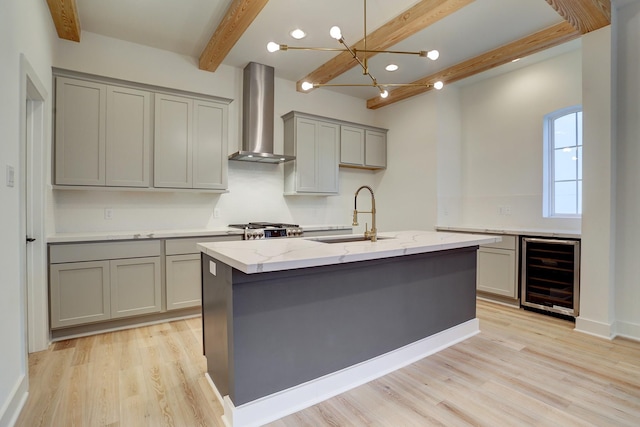 kitchen featuring wall chimney exhaust hood, sink, gray cabinetry, light stone counters, and beverage cooler